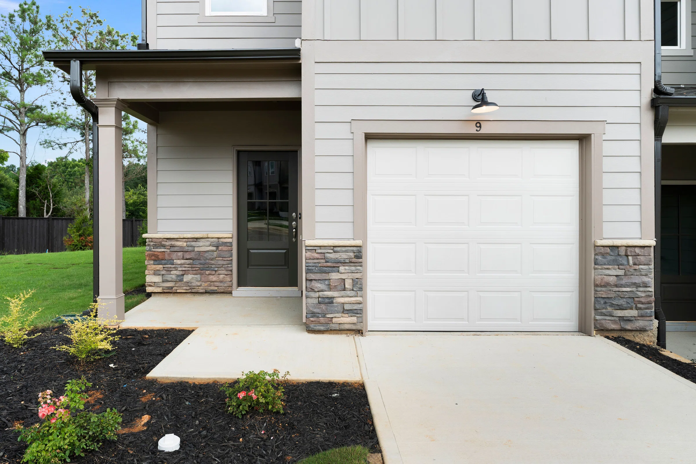 Front view of a modern house with a single-car garage, covered entryway, stone accents, and landscaped yard with small plants.