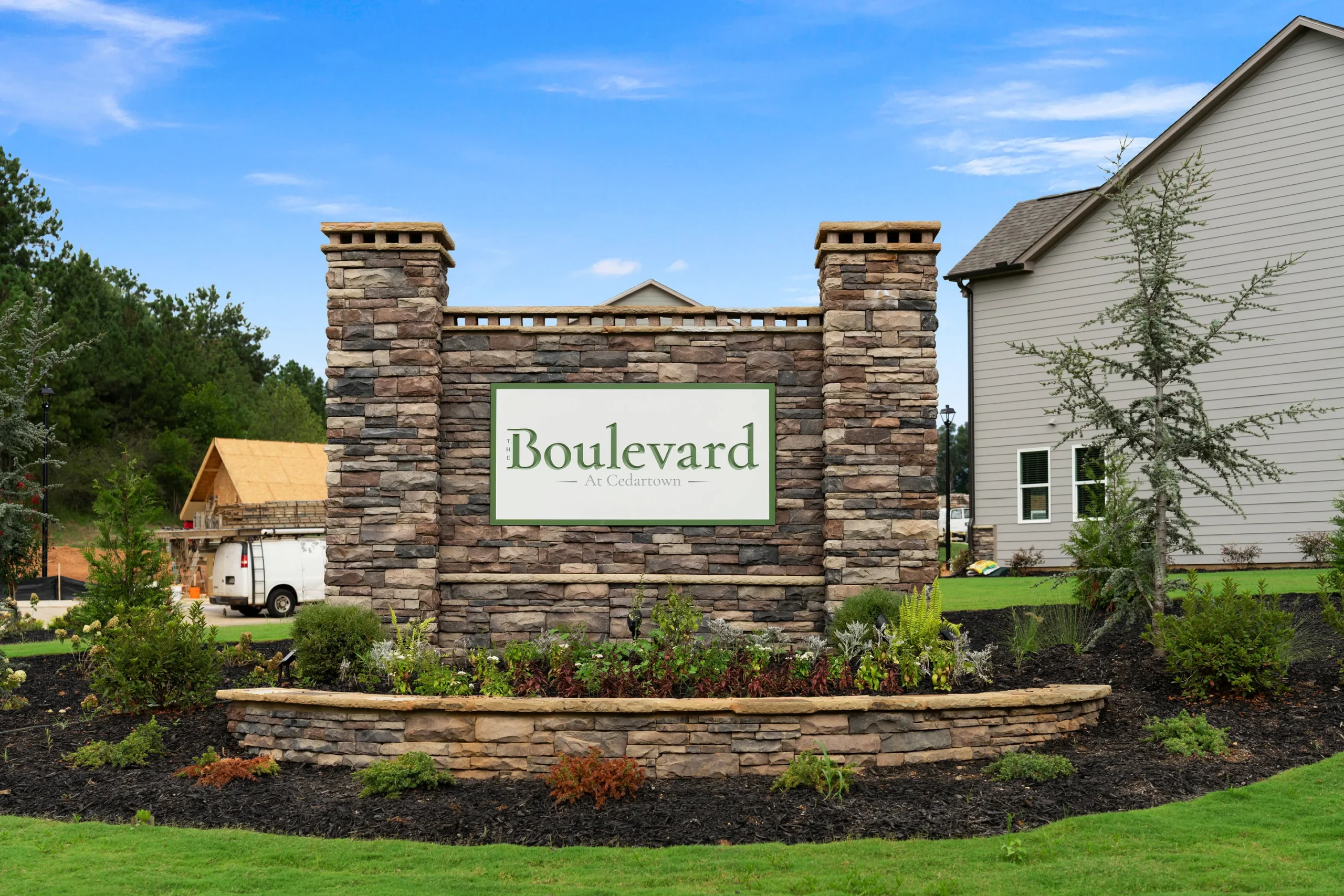 Stone entrance sign reads “Boulevard at Cochrans” surrounded by landscaping, with houses and a construction site visible in the background on a sunny day.