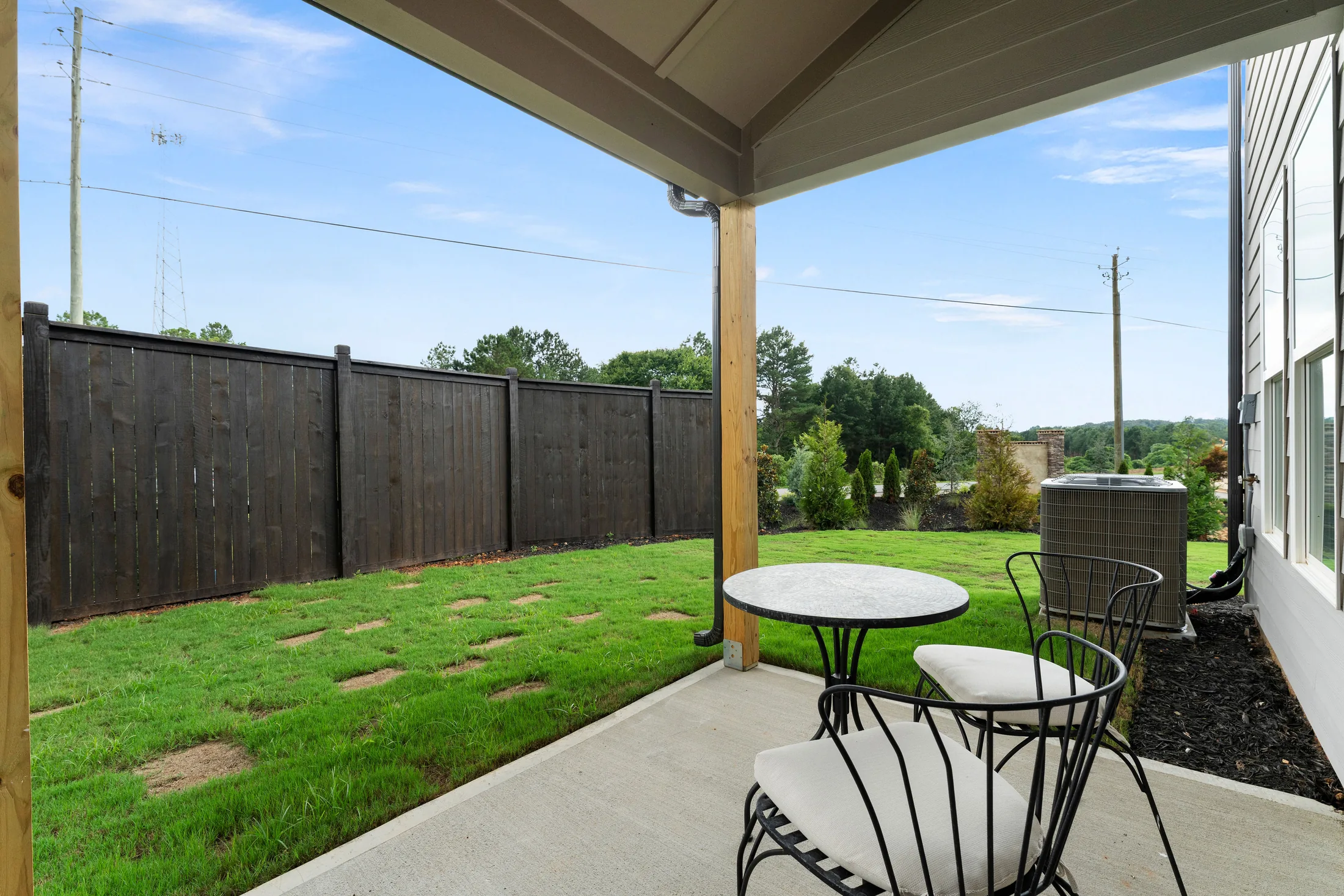 A covered patio with a small metal table and two chairs overlooking a fenced backyard, highlighting the residential features of this community.