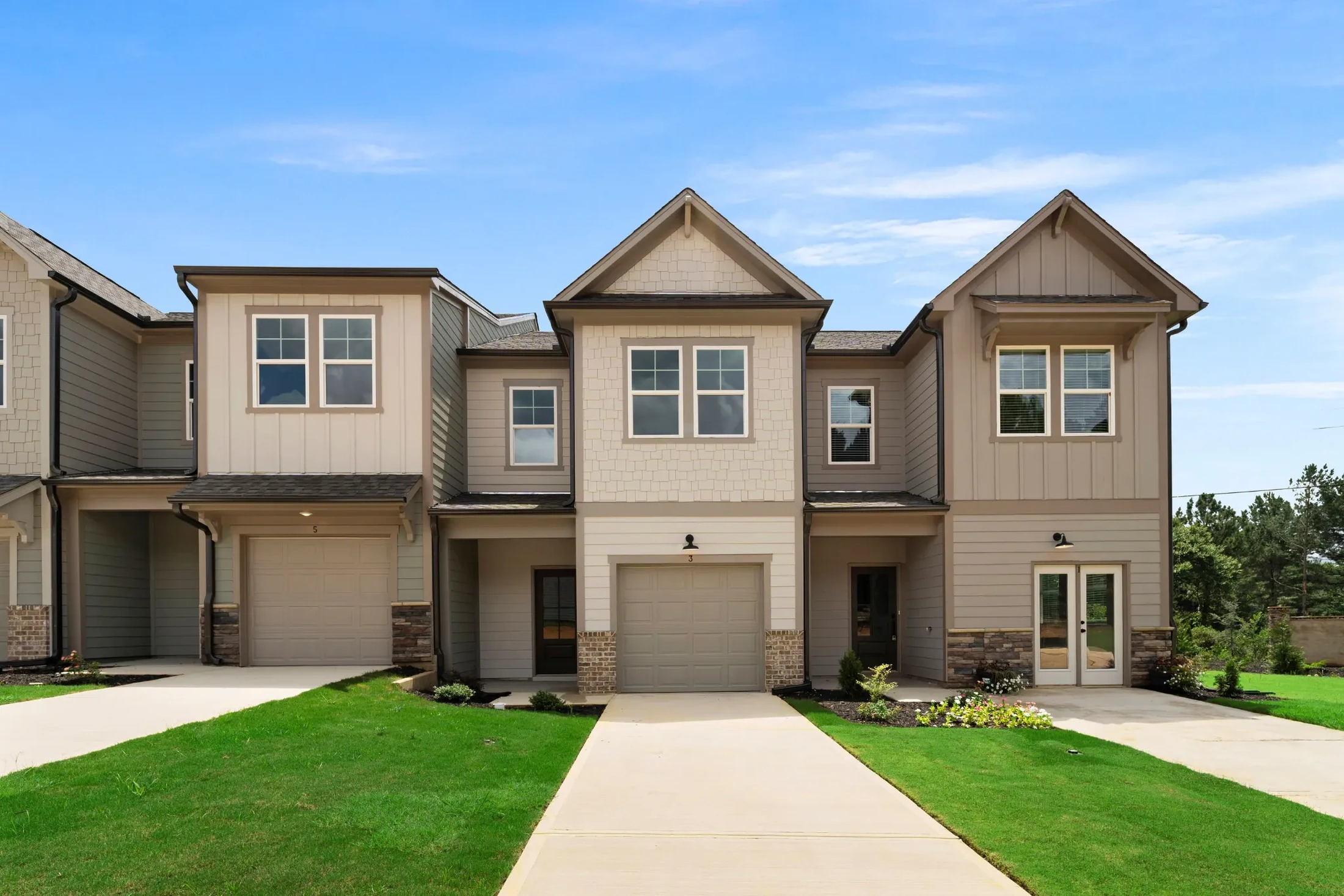 Three adjacent multi-story townhomes with beige siding, garages, and concrete driveways, reflecting typical residential features of the community.