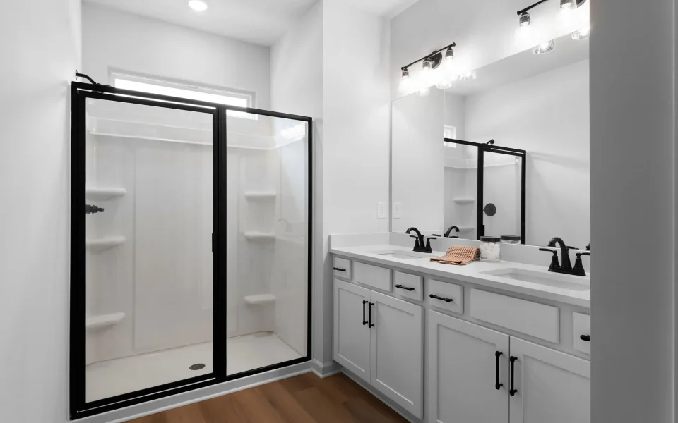 A modern bathroom featuring a white shower stall with a black frame, a double vanity with white cabinets and black hardware, and a large wall mirror.