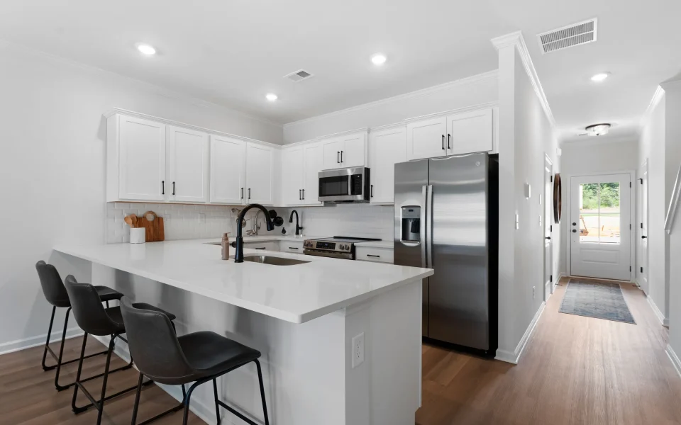 Modern kitchen with white cabinets, stainless steel appliances, and a quartz island with three black stools.