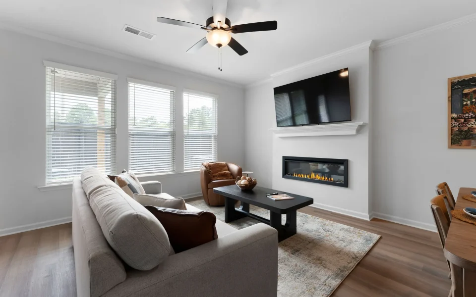 Living room with a sofa, leather armchair, black coffee table, and a wall-mounted fireplace and television.