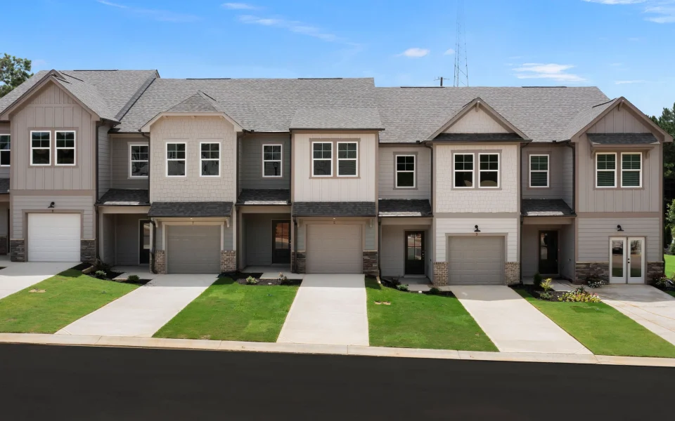 A row of five attached townhouse units with gray siding, shingled roofs, individual garages, and concrete driveways.